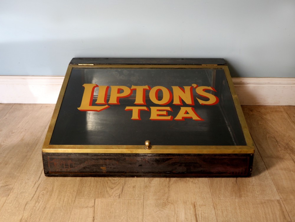A low profile glass countertop display cabinet with a brass frame and yellow and red lettering reading Liptons Tea on a black background. View II