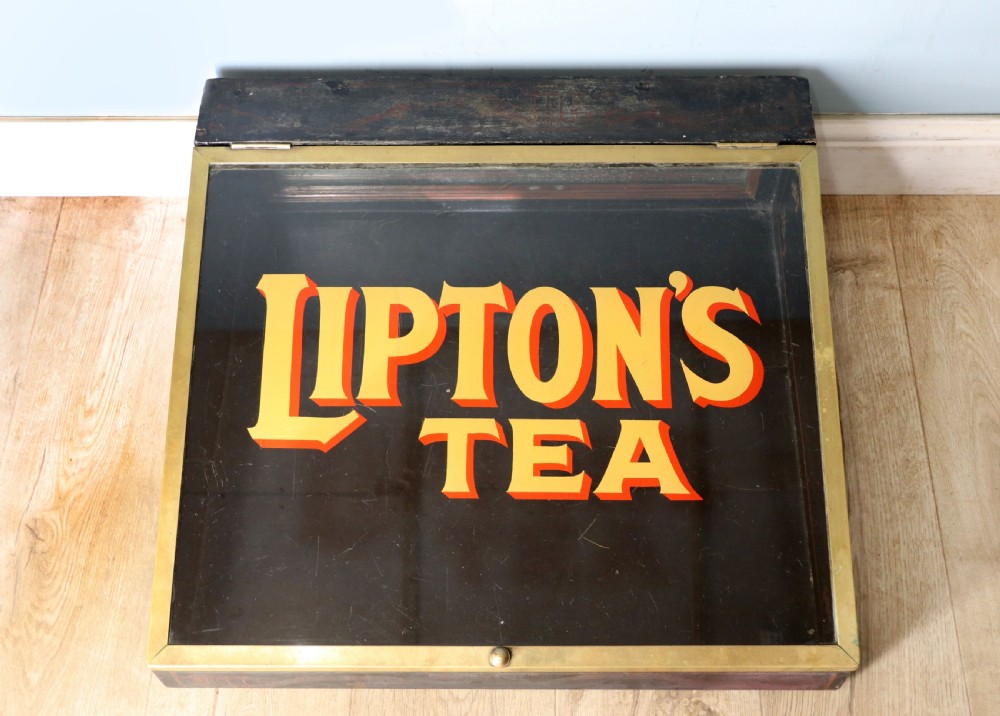 A low profile glass countertop display cabinet with a brass frame and yellow and red lettering reading Liptons Tea on a black background.