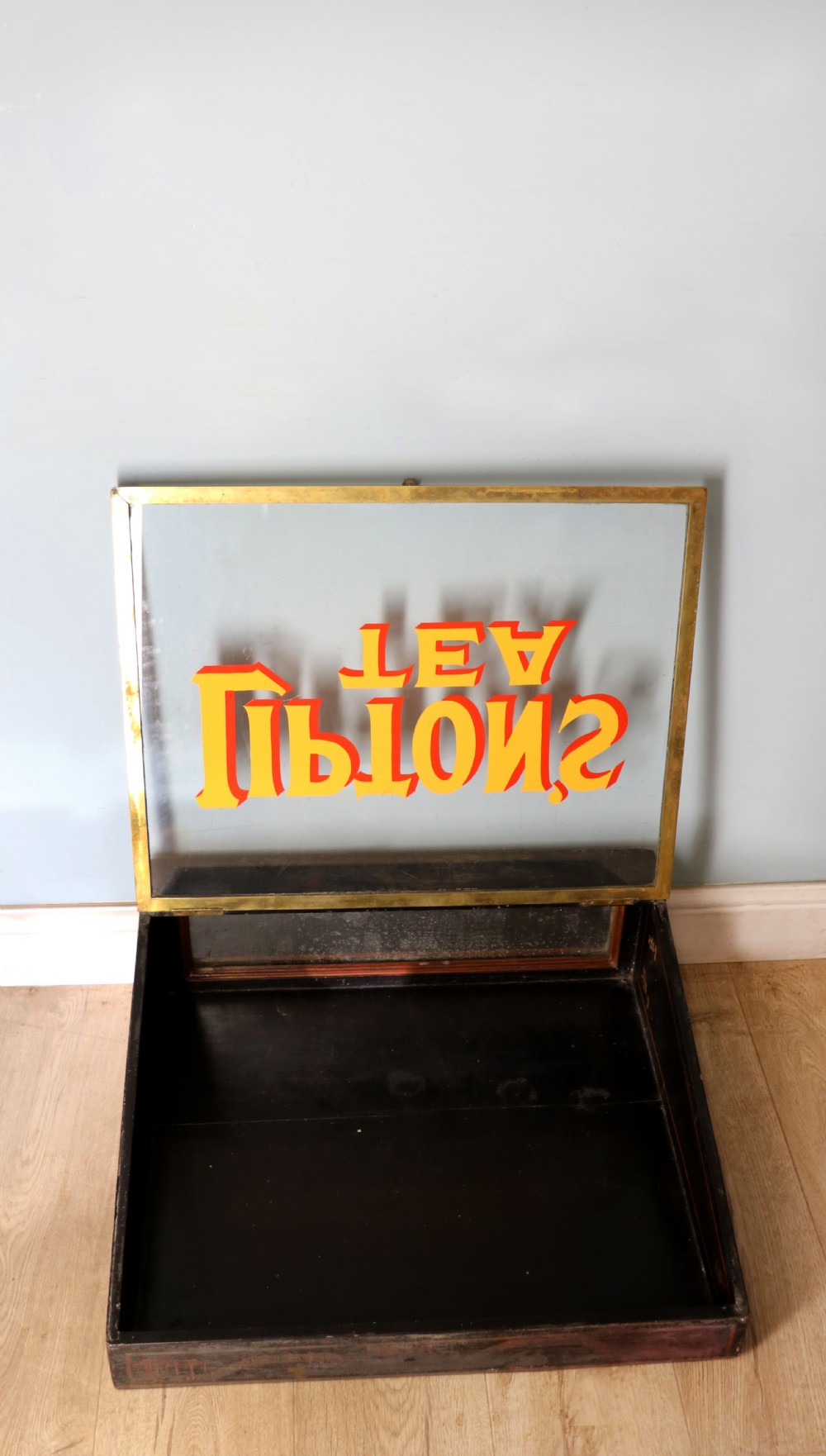 A low profile glass countertop display cabinet with a brass frame and yellow and red lettering reading Liptons Tea on a black background. View IV