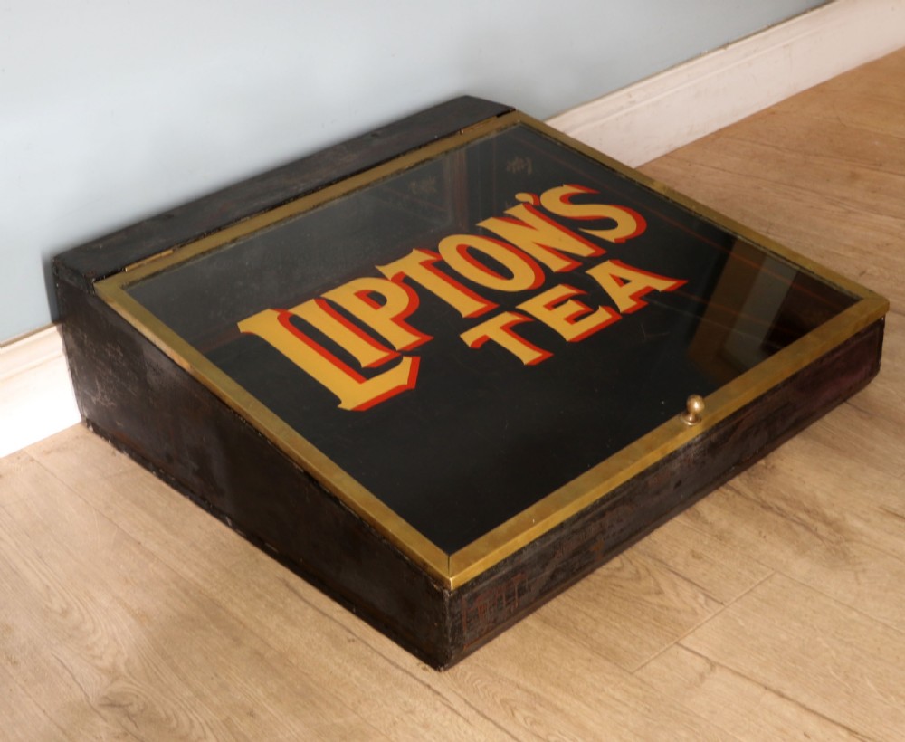 A low profile glass countertop display cabinet with a brass frame and yellow and red lettering reading Liptons Tea on a black background. View V