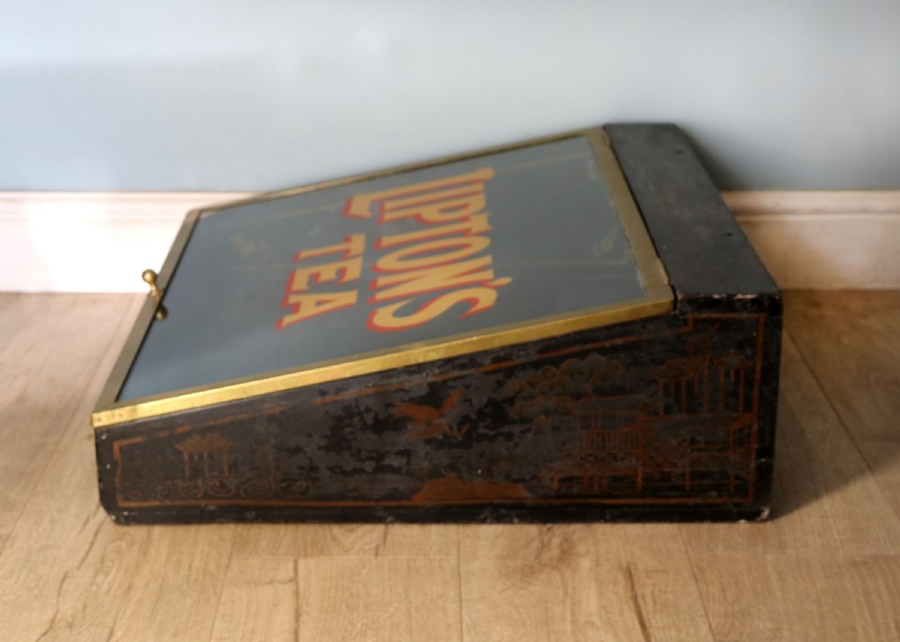 A low profile glass countertop display cabinet with a brass frame and yellow and red lettering reading Liptons Tea on a black background. View VI