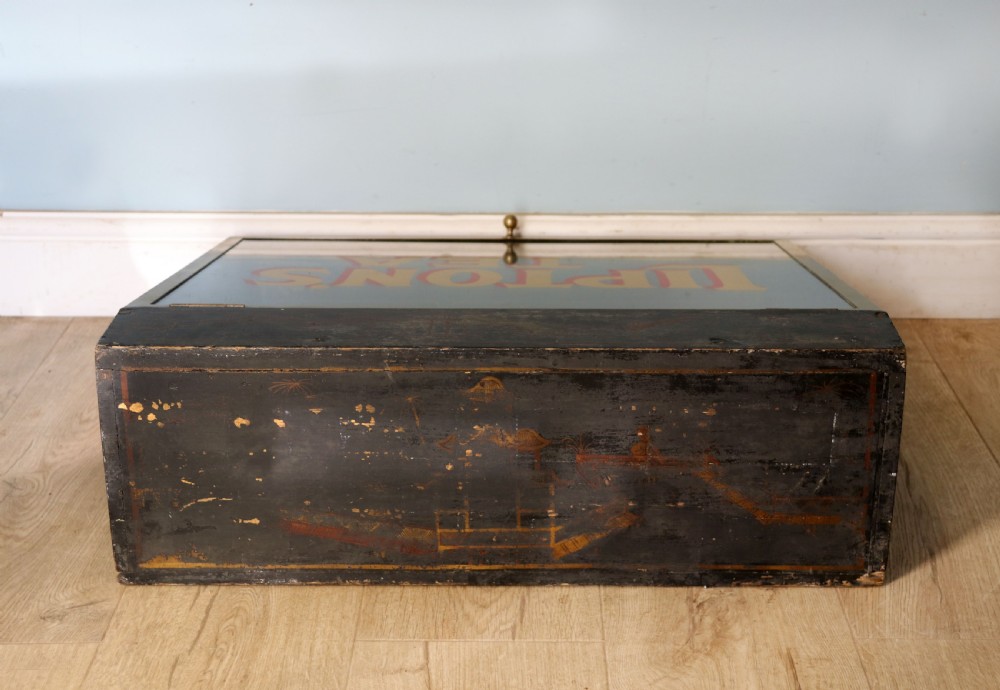 A low profile glass countertop display cabinet with a brass frame and yellow and red lettering reading Liptons Tea on a black background. View VII