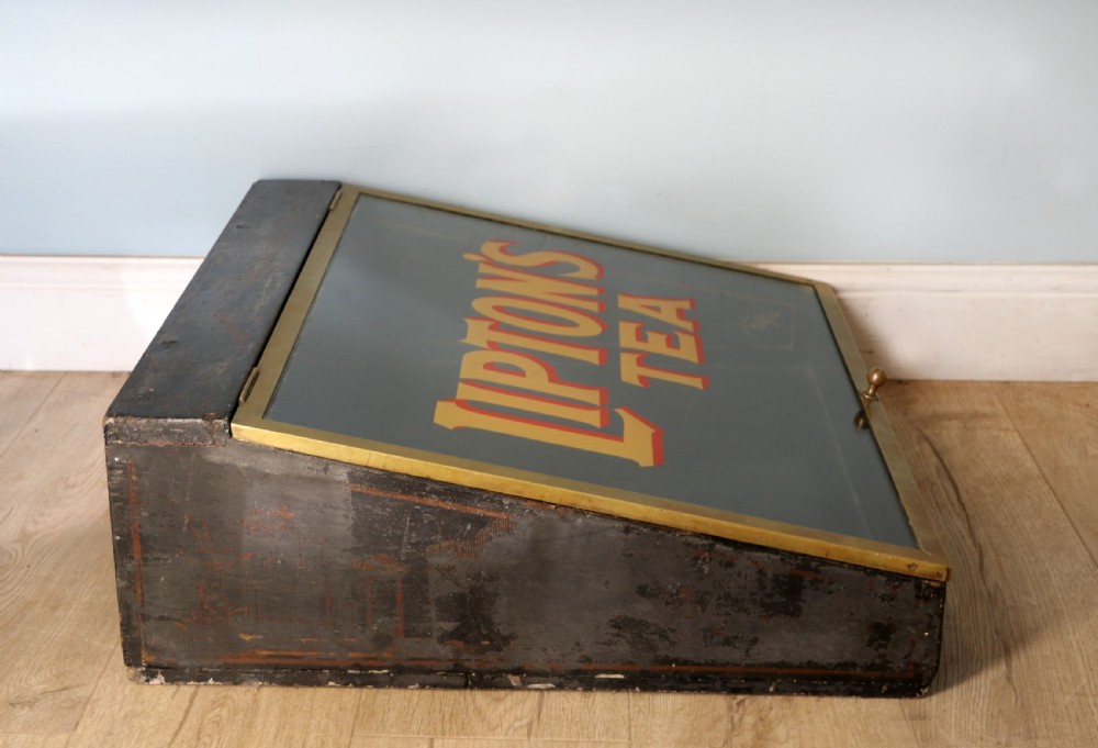 A low profile glass countertop display cabinet with a brass frame and yellow and red lettering reading Liptons Tea on a black background. View VIII