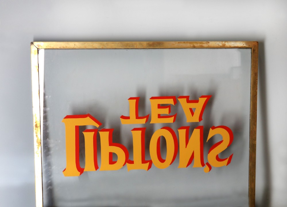 A low profile glass countertop display cabinet with a brass frame and yellow and red lettering reading Liptons Tea on a black background. View IX