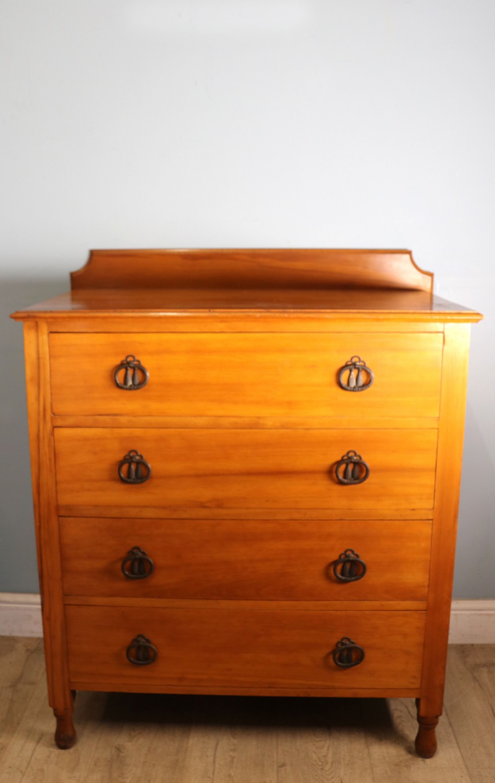 A late Victorian American walnut chest of drawers featuring four full-width drawers with metal drop-ring handles, a low shaped gallery upstand, and turned feet.