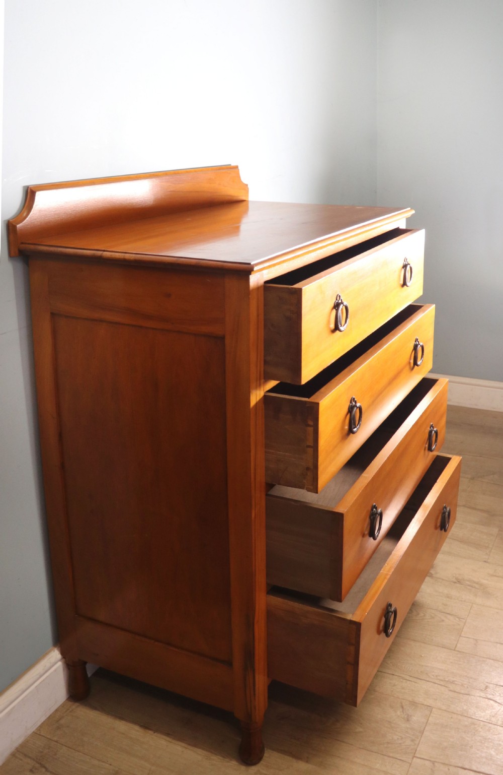 A late Victorian American walnut chest of drawers featuring four full-width drawers with metal drop-ring handles, a low shaped gallery upstand, and turned feet. View IV