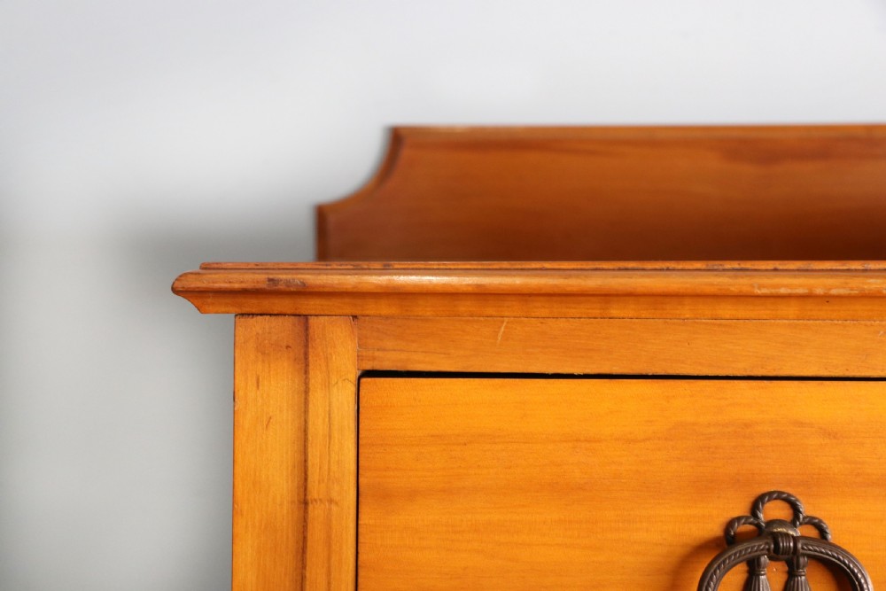 A late Victorian American walnut chest of drawers featuring four full-width drawers with metal drop-ring handles, a low shaped gallery upstand, and turned feet. View V