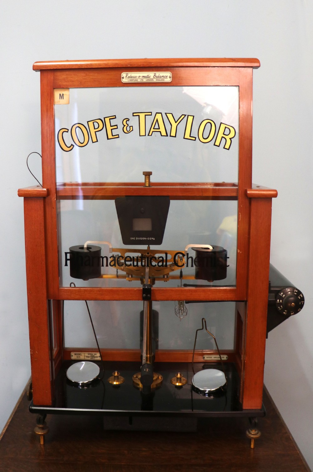 An Oertling precision chemists beam balance scale with a brass mechanism housed inside a glazed timber cabinet featuring gilded gold typography. View III