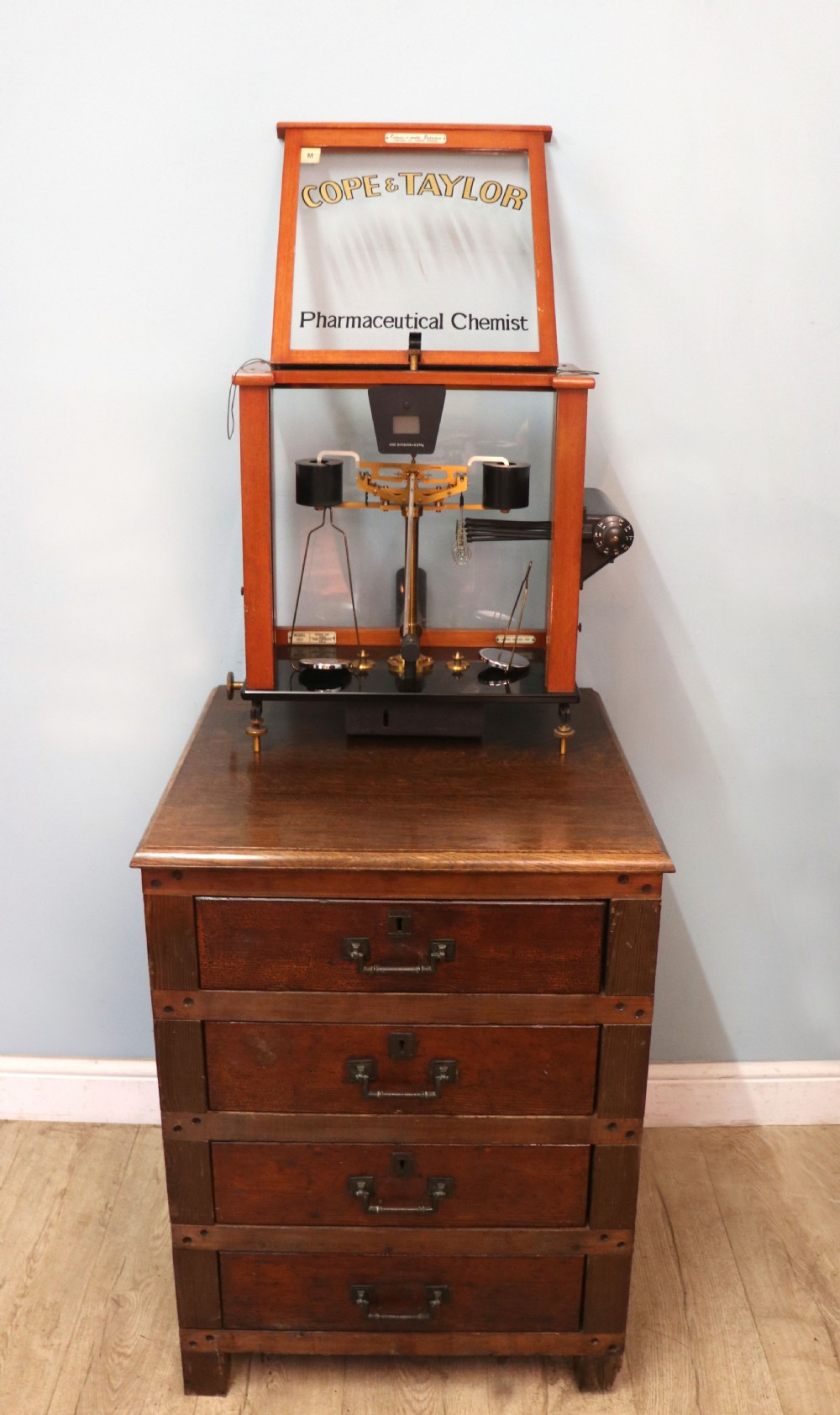 An Oertling precision chemists beam balance scale with a brass mechanism housed inside a glazed timber cabinet featuring gilded gold typography. View IV