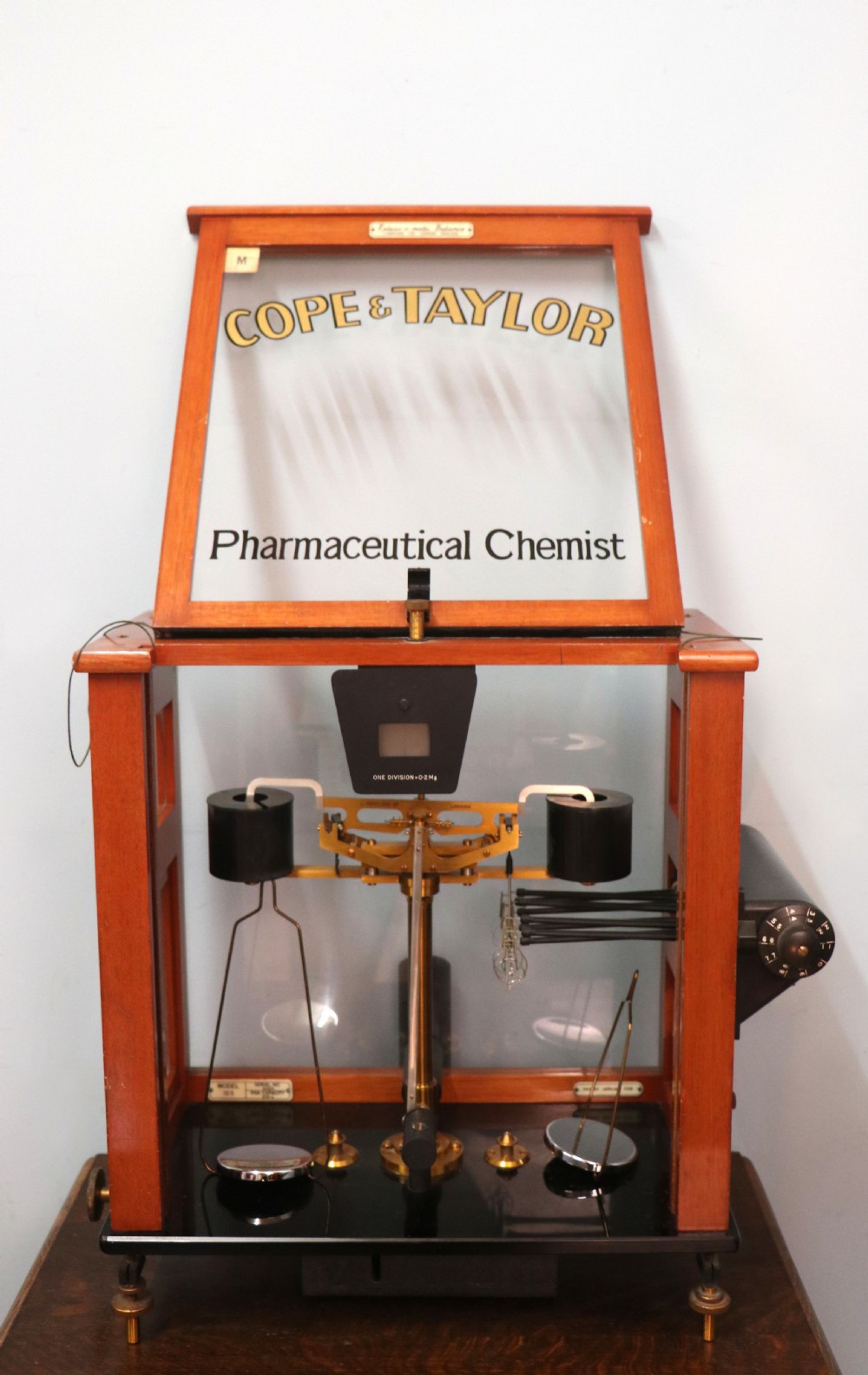 An Oertling precision chemists beam balance scale with a brass mechanism housed inside a glazed timber cabinet featuring gilded gold typography. View V