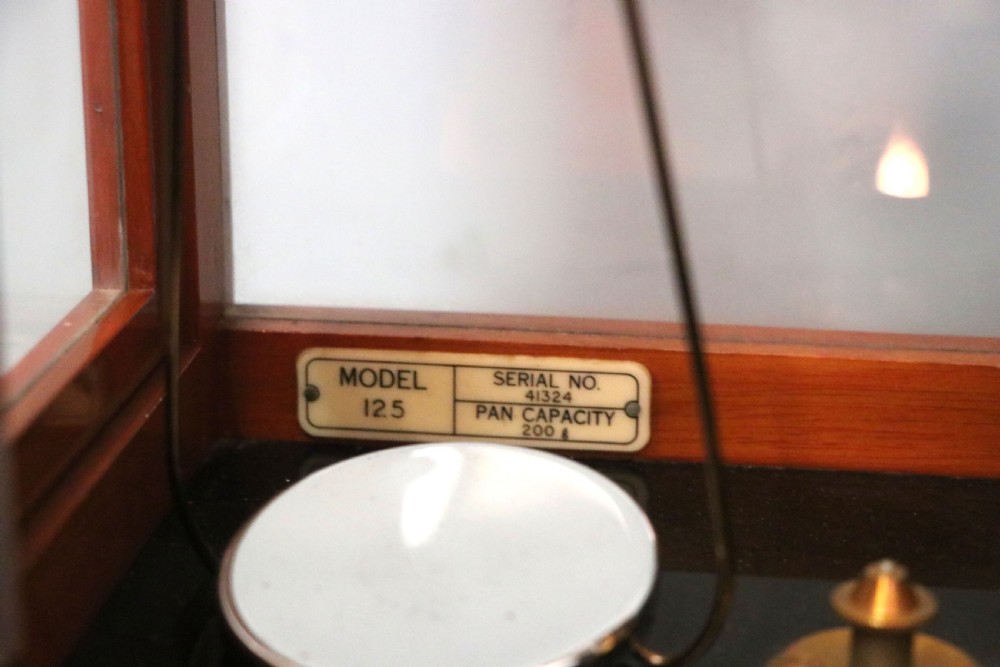 An Oertling precision chemists beam balance scale with a brass mechanism housed inside a glazed timber cabinet featuring gilded gold typography. View VII