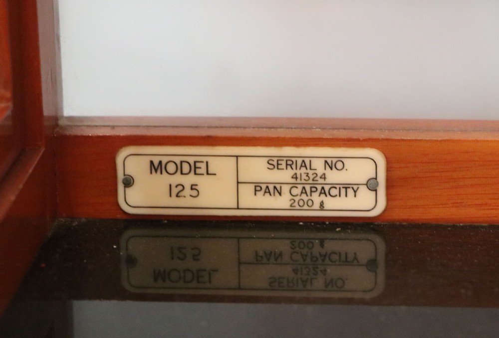 An Oertling precision chemists beam balance scale with a brass mechanism housed inside a glazed timber cabinet featuring gilded gold typography. View VIII