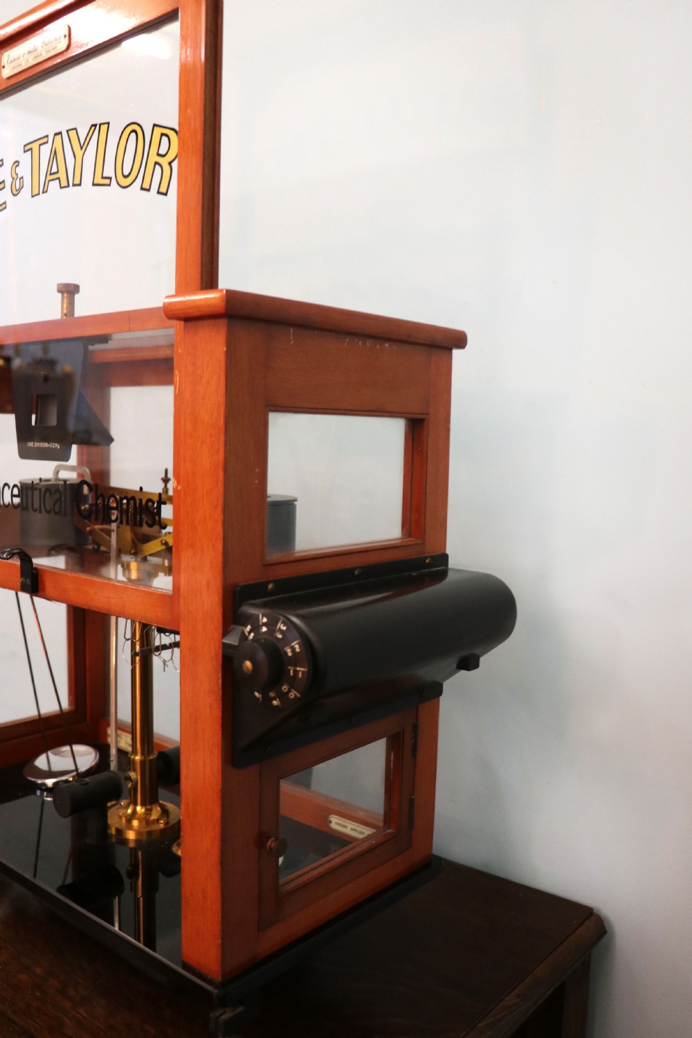 An Oertling precision chemists beam balance scale with a brass mechanism housed inside a glazed timber cabinet featuring gilded gold typography. View X