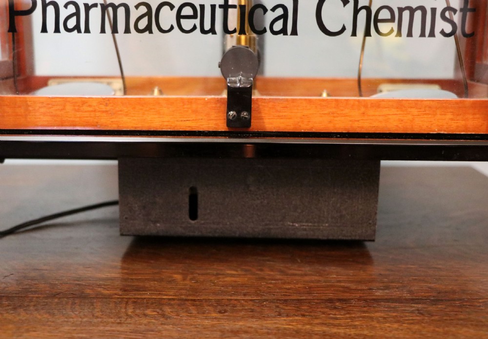 An Oertling precision chemists beam balance scale with a brass mechanism housed inside a glazed timber cabinet featuring gilded gold typography. View XVIII