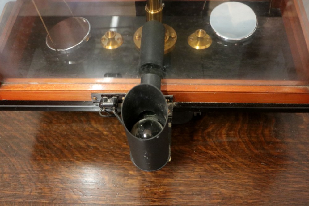 An Oertling precision chemists beam balance scale with a brass mechanism housed inside a glazed timber cabinet featuring gilded gold typography. View XX