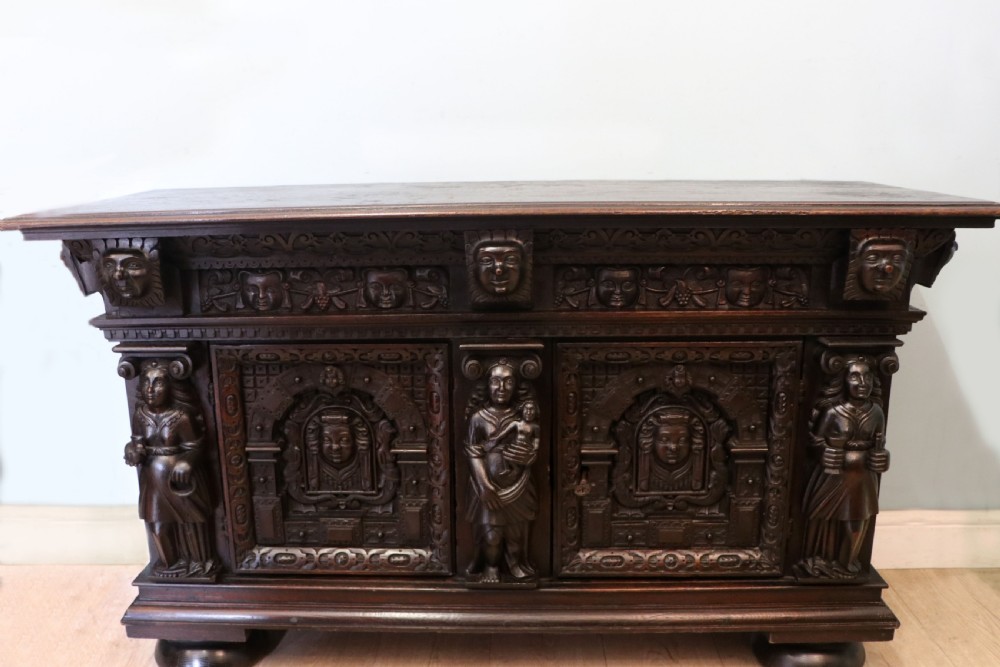 A dark carved Flemish oak side cabinet featuring detailed figural caryatids, relief mascarons, architectural door panels, and heavy bun feet. View II
