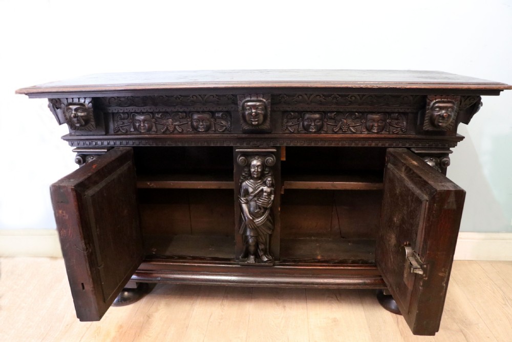 A dark carved Flemish oak side cabinet featuring detailed figural caryatids, relief mascarons, architectural door panels, and heavy bun feet. View III