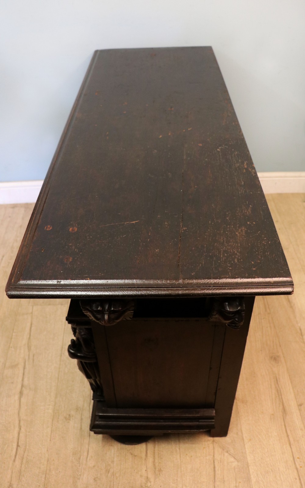 A dark carved Flemish oak side cabinet featuring detailed figural caryatids, relief mascarons, architectural door panels, and heavy bun feet. View V