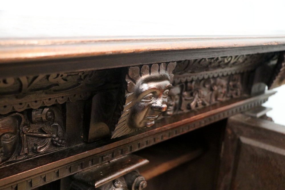 A dark carved Flemish oak side cabinet featuring detailed figural caryatids, relief mascarons, architectural door panels, and heavy bun feet. View VII
