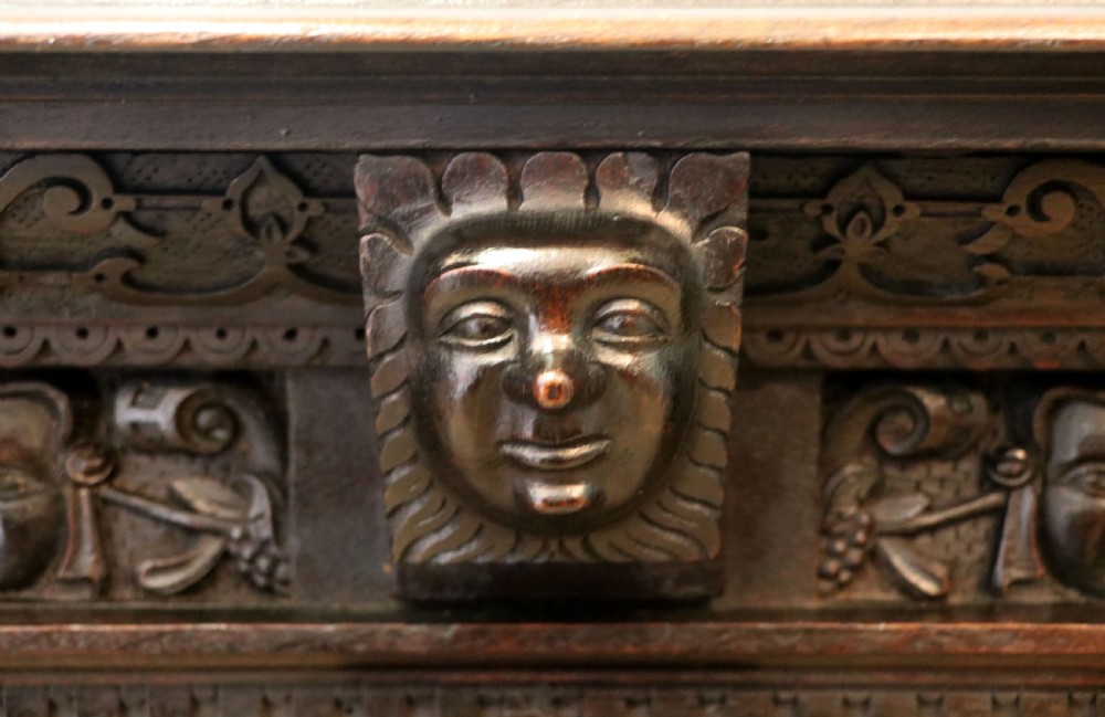 A dark carved Flemish oak side cabinet featuring detailed figural caryatids, relief mascarons, architectural door panels, and heavy bun feet. View X