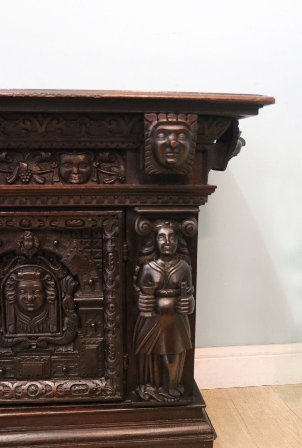 A dark carved Flemish oak side cabinet featuring detailed figural caryatids, relief mascarons, architectural door panels, and heavy bun feet. View XI