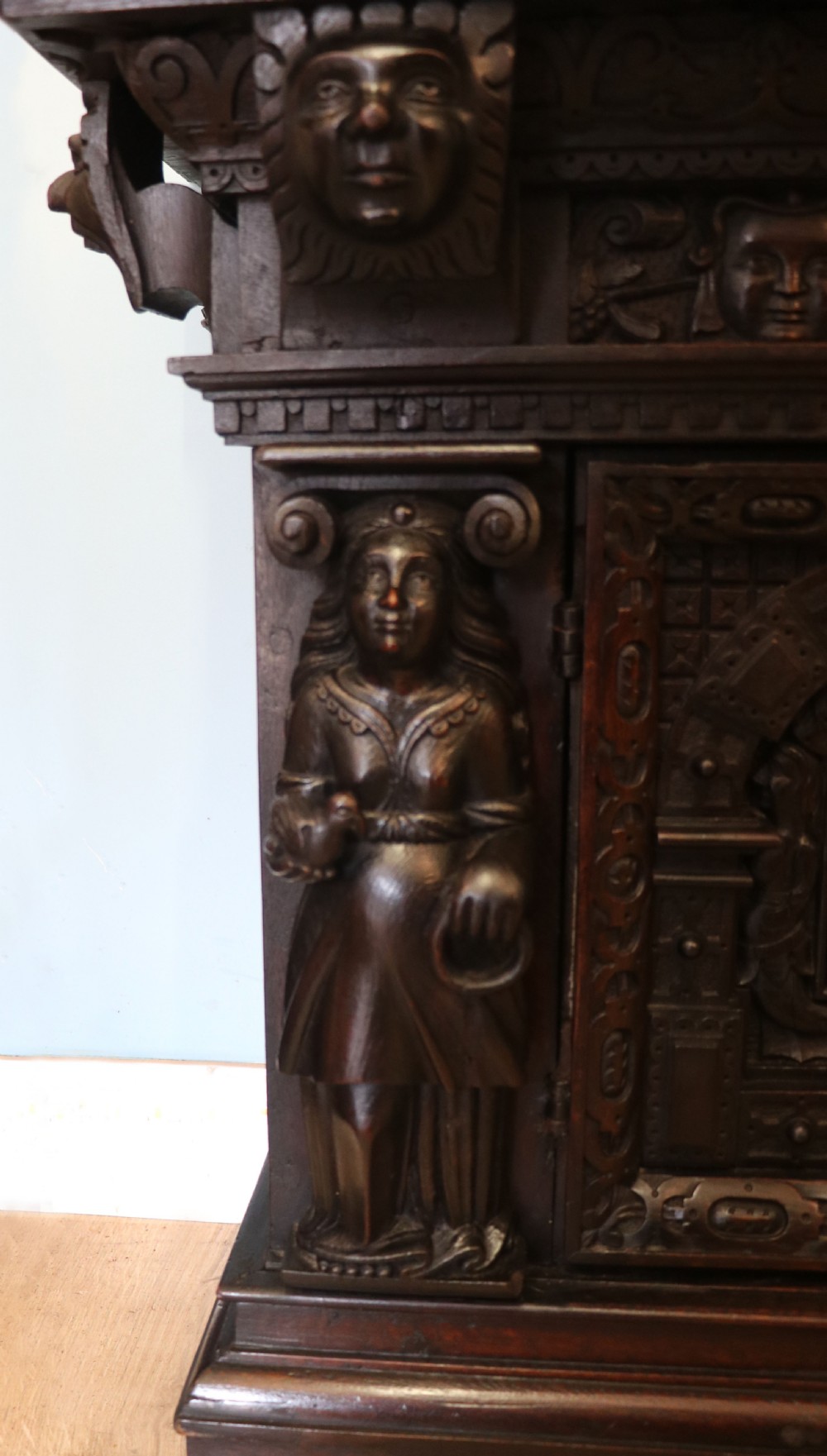 A dark carved Flemish oak side cabinet featuring detailed figural caryatids, relief mascarons, architectural door panels, and heavy bun feet. View XII