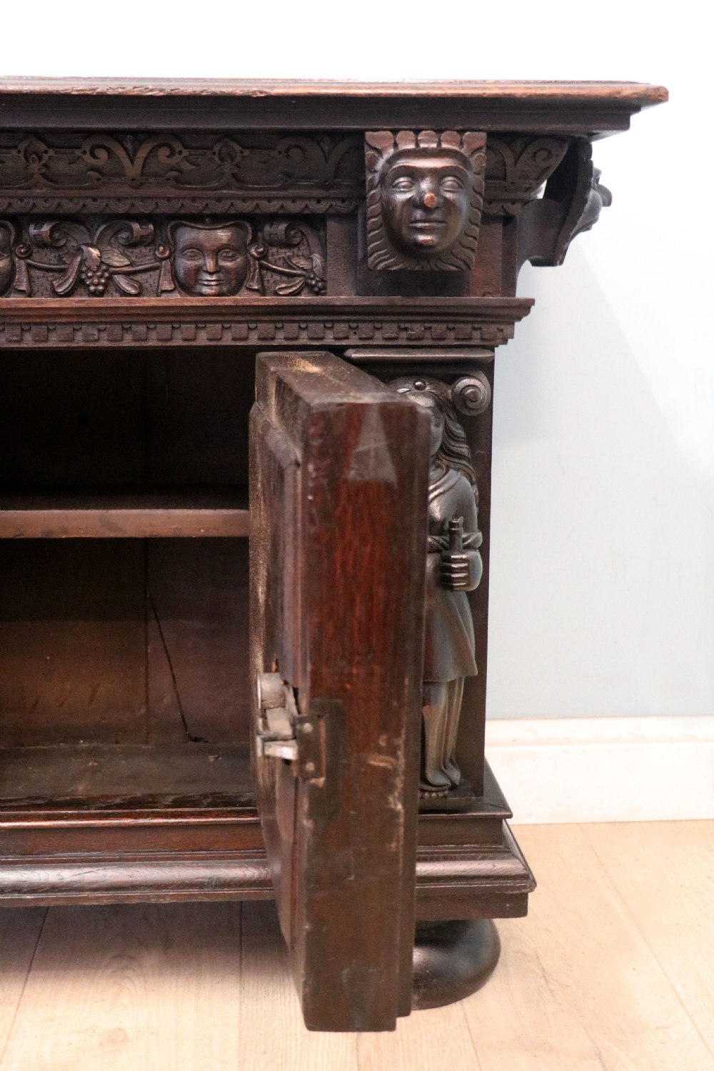 A dark carved Flemish oak side cabinet featuring detailed figural caryatids, relief mascarons, architectural door panels, and heavy bun feet. View XIV