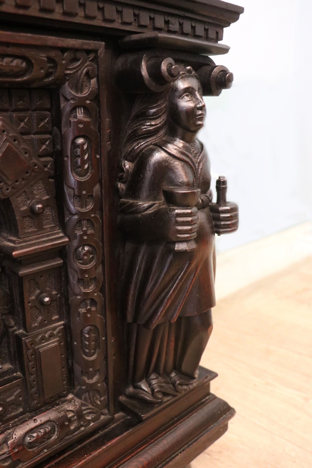 A dark carved Flemish oak side cabinet featuring detailed figural caryatids, relief mascarons, architectural door panels, and heavy bun feet. View XVIII