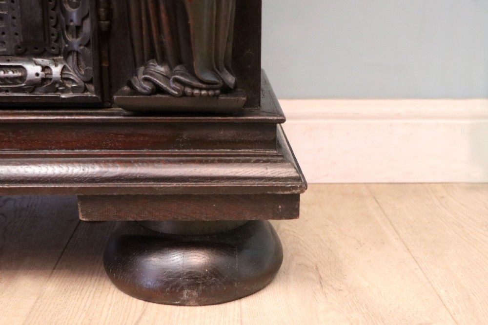 A dark carved Flemish oak side cabinet featuring detailed figural caryatids, relief mascarons, architectural door panels, and heavy bun feet. View XXII
