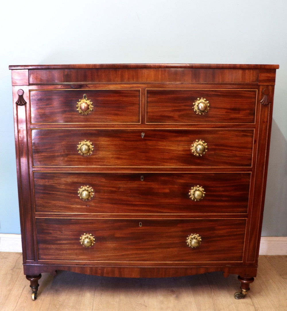 A nineteenth-century flame mahogany chest of drawers with two short and three long graduated drawers, decorative brass handles, and turned legs on castors.