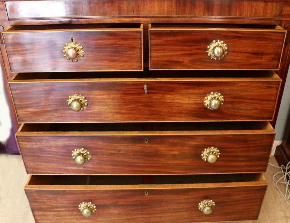 A nineteenth-century flame mahogany chest of drawers with two short and three long graduated drawers, decorative brass handles, and turned legs on castors. View II