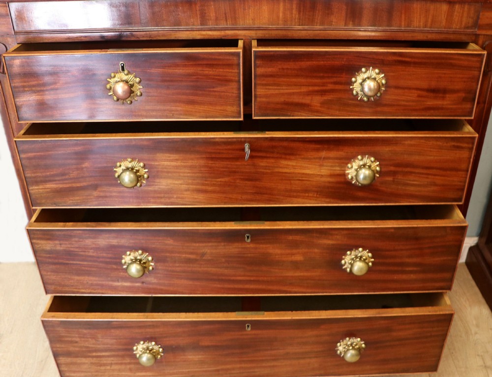 A nineteenth-century flame mahogany chest of drawers with two short and three long graduated drawers, decorative brass handles, and turned legs on castors. View III
