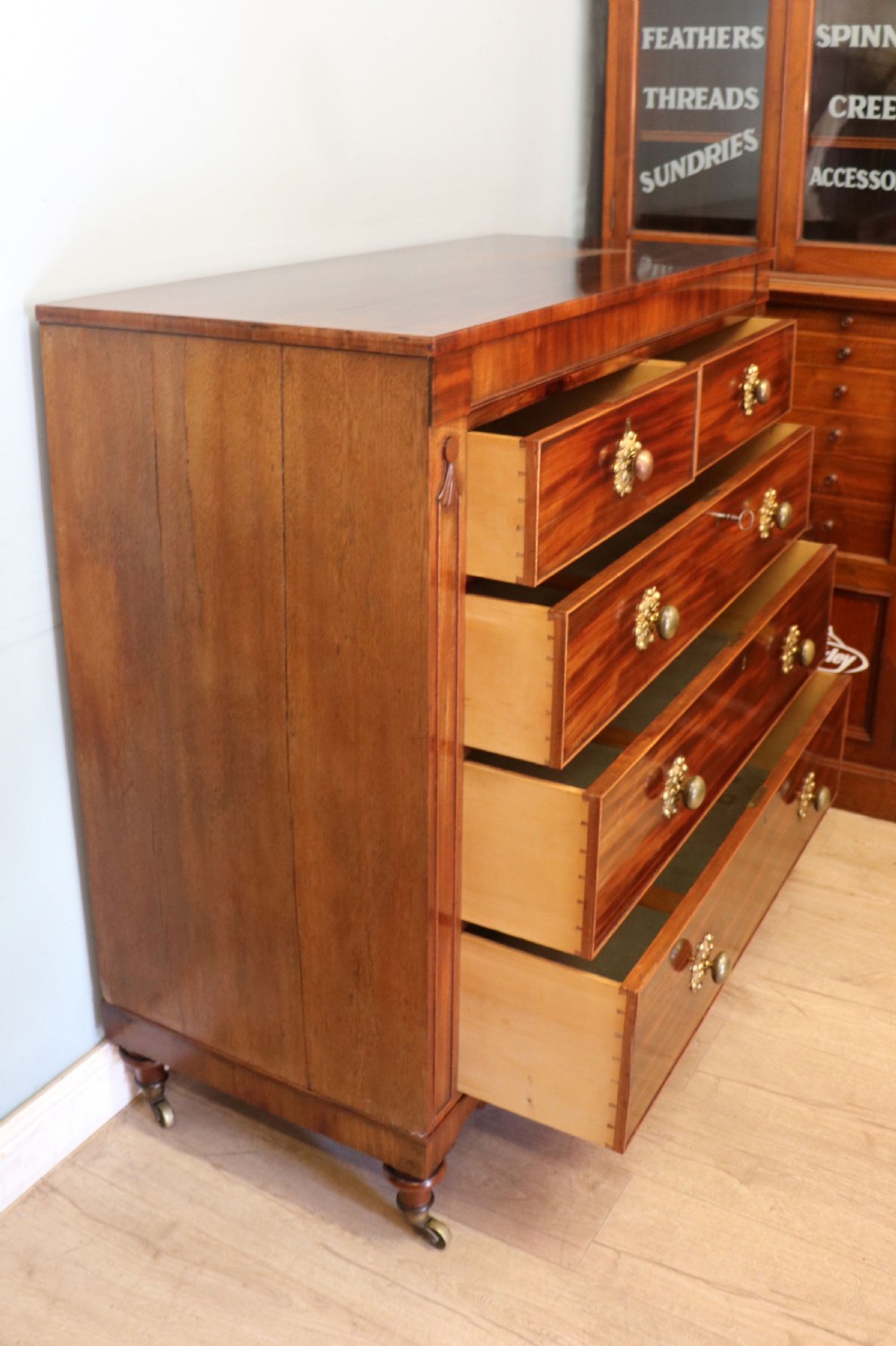 A nineteenth-century flame mahogany chest of drawers with two short and three long graduated drawers, decorative brass handles, and turned legs on castors. View V