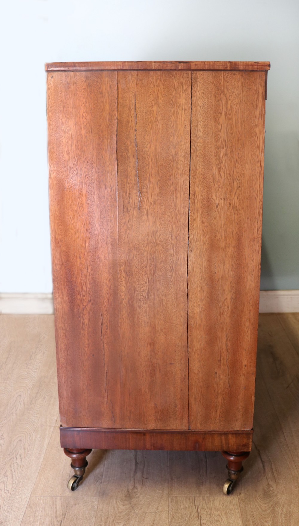 A nineteenth-century flame mahogany chest of drawers with two short and three long graduated drawers, decorative brass handles, and turned legs on castors. View VI