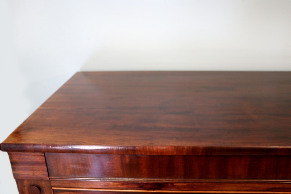 A nineteenth-century flame mahogany chest of drawers with two short and three long graduated drawers, decorative brass handles, and turned legs on castors. View VII