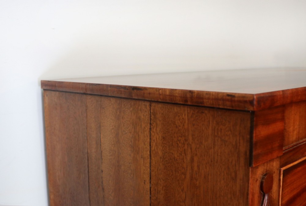 A nineteenth-century flame mahogany chest of drawers with two short and three long graduated drawers, decorative brass handles, and turned legs on castors. View VIII
