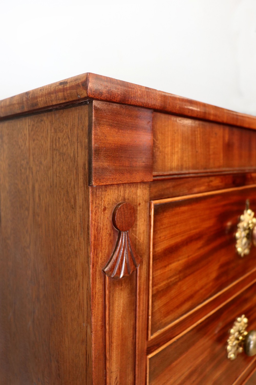A nineteenth-century flame mahogany chest of drawers with two short and three long graduated drawers, decorative brass handles, and turned legs on castors. View X