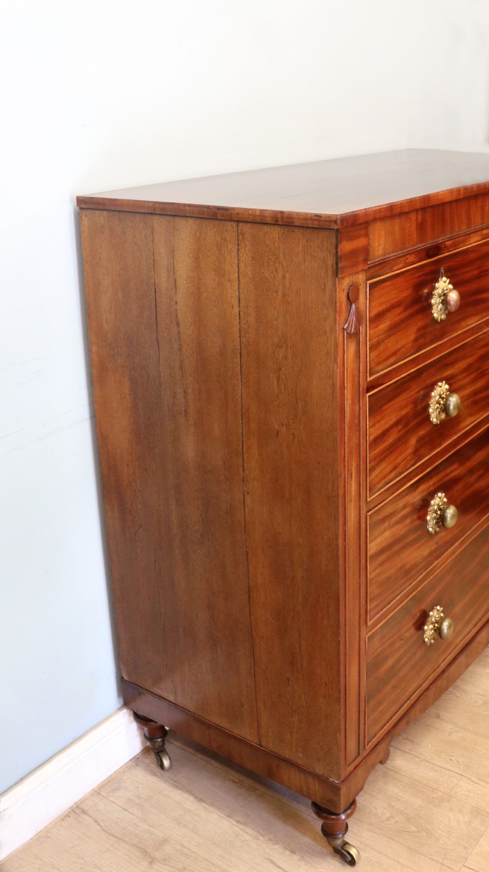 A nineteenth-century flame mahogany chest of drawers with two short and three long graduated drawers, decorative brass handles, and turned legs on castors. View XI