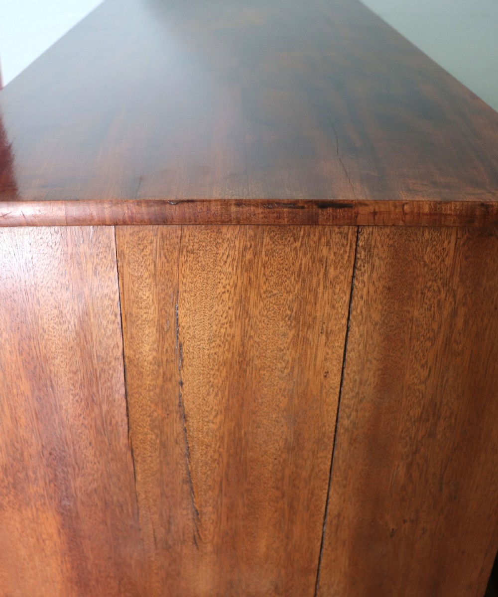 A nineteenth-century flame mahogany chest of drawers with two short and three long graduated drawers, decorative brass handles, and turned legs on castors. View XII