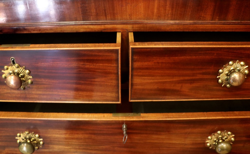A nineteenth-century flame mahogany chest of drawers with two short and three long graduated drawers, decorative brass handles, and turned legs on castors. View XIV