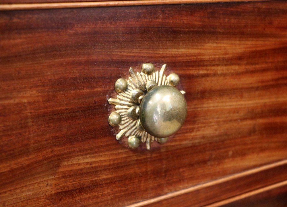 A nineteenth-century flame mahogany chest of drawers with two short and three long graduated drawers, decorative brass handles, and turned legs on castors. View XVII