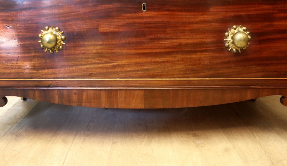 A nineteenth-century flame mahogany chest of drawers with two short and three long graduated drawers, decorative brass handles, and turned legs on castors. View XXI
