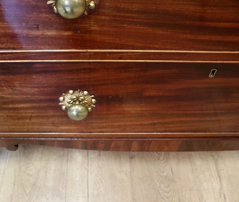 A nineteenth-century flame mahogany chest of drawers with two short and three long graduated drawers, decorative brass handles, and turned legs on castors. View XXII
