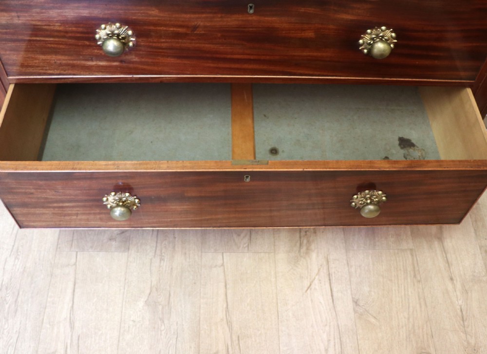 A nineteenth-century flame mahogany chest of drawers with two short and three long graduated drawers, decorative brass handles, and turned legs on castors. View XXIII