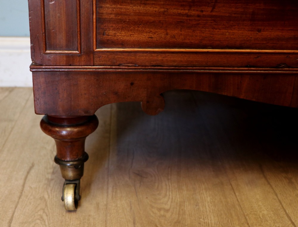 A nineteenth-century flame mahogany chest of drawers with two short and three long graduated drawers, decorative brass handles, and turned legs on castors. View XXIV