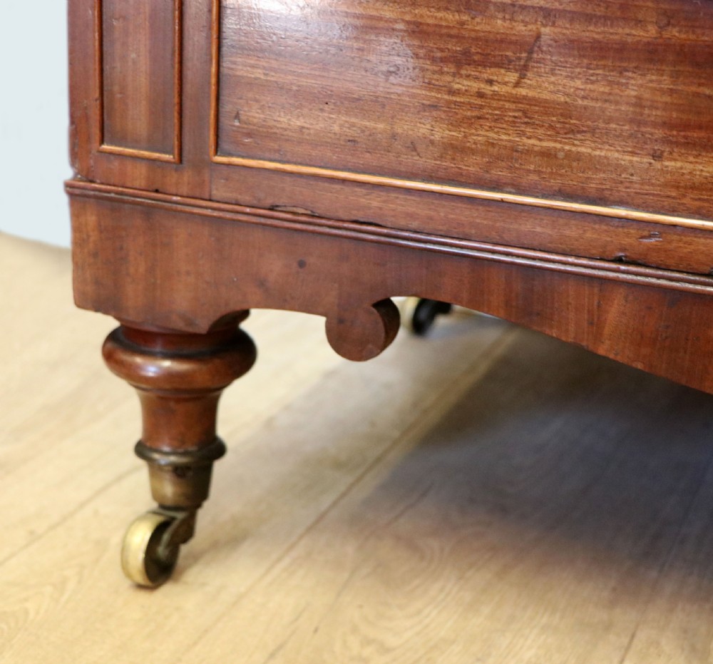 A nineteenth-century flame mahogany chest of drawers with two short and three long graduated drawers, decorative brass handles, and turned legs on castors. View XXV