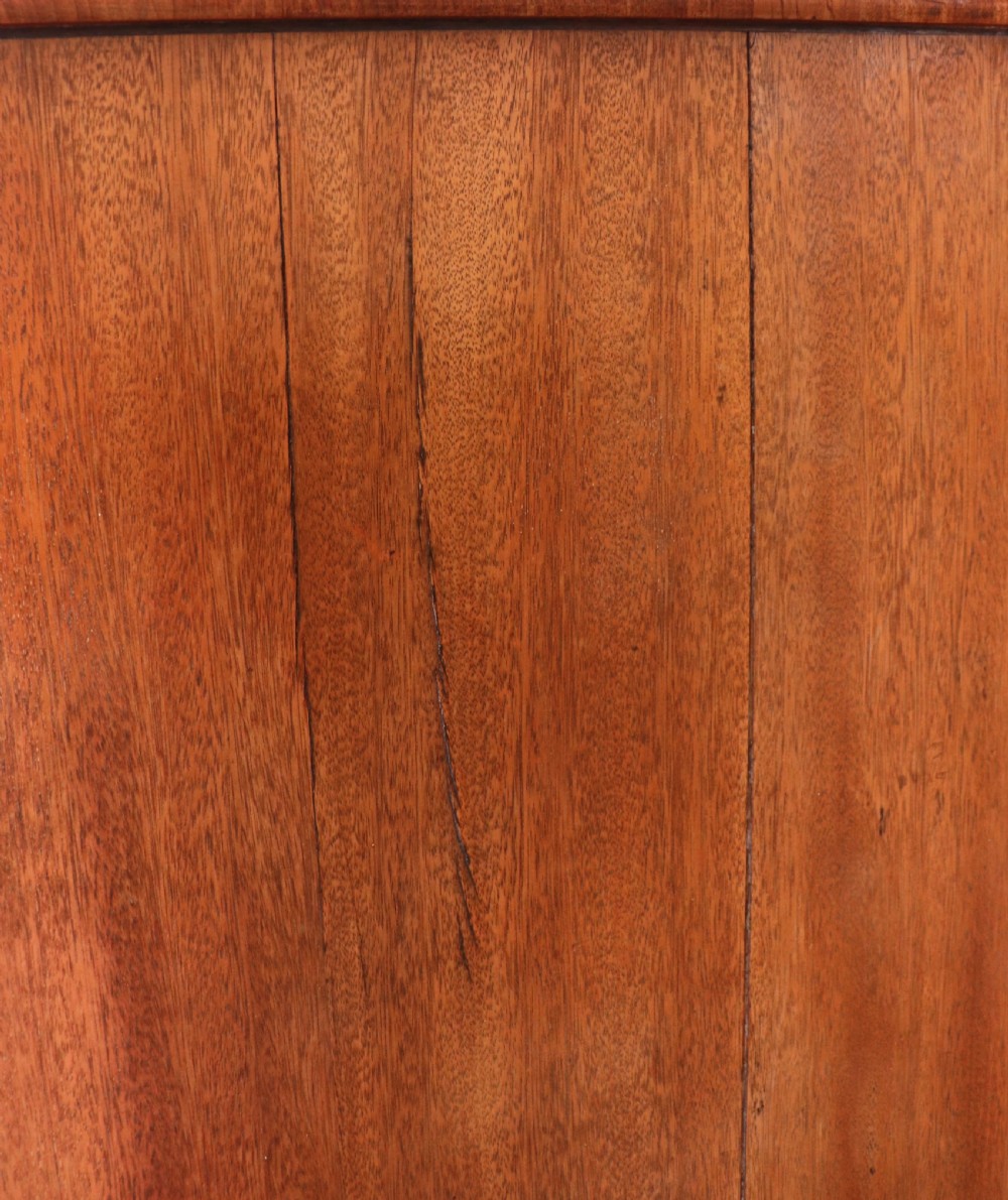 A nineteenth-century flame mahogany chest of drawers with two short and three long graduated drawers, decorative brass handles, and turned legs on castors. View XXVI
