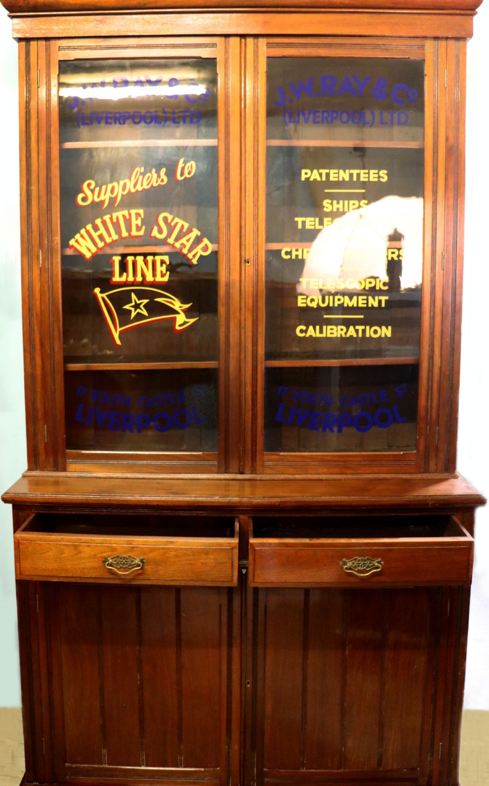 A late 19th-century walnut glazed display cabinet featuring two glass doors decorated with gilded signwriting above two drawers and a panelled base cupboard.