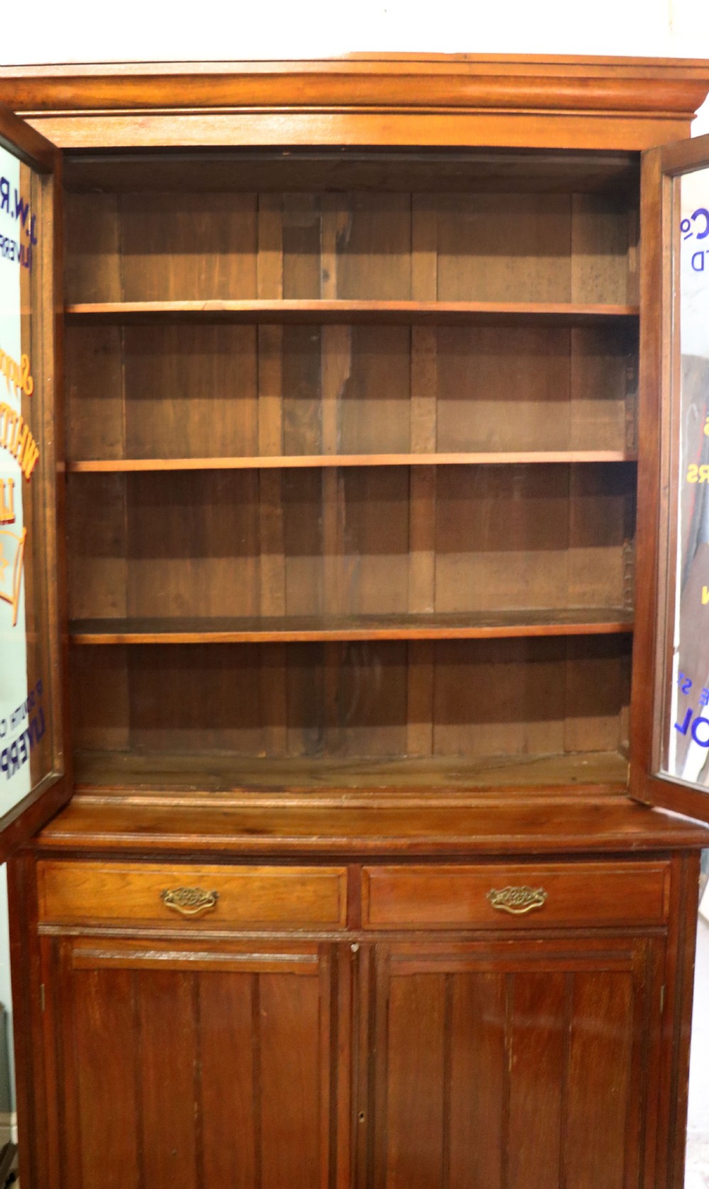 A late 19th-century walnut glazed display cabinet featuring two glass doors decorated with gilded signwriting above two drawers and a panelled base cupboard. View X