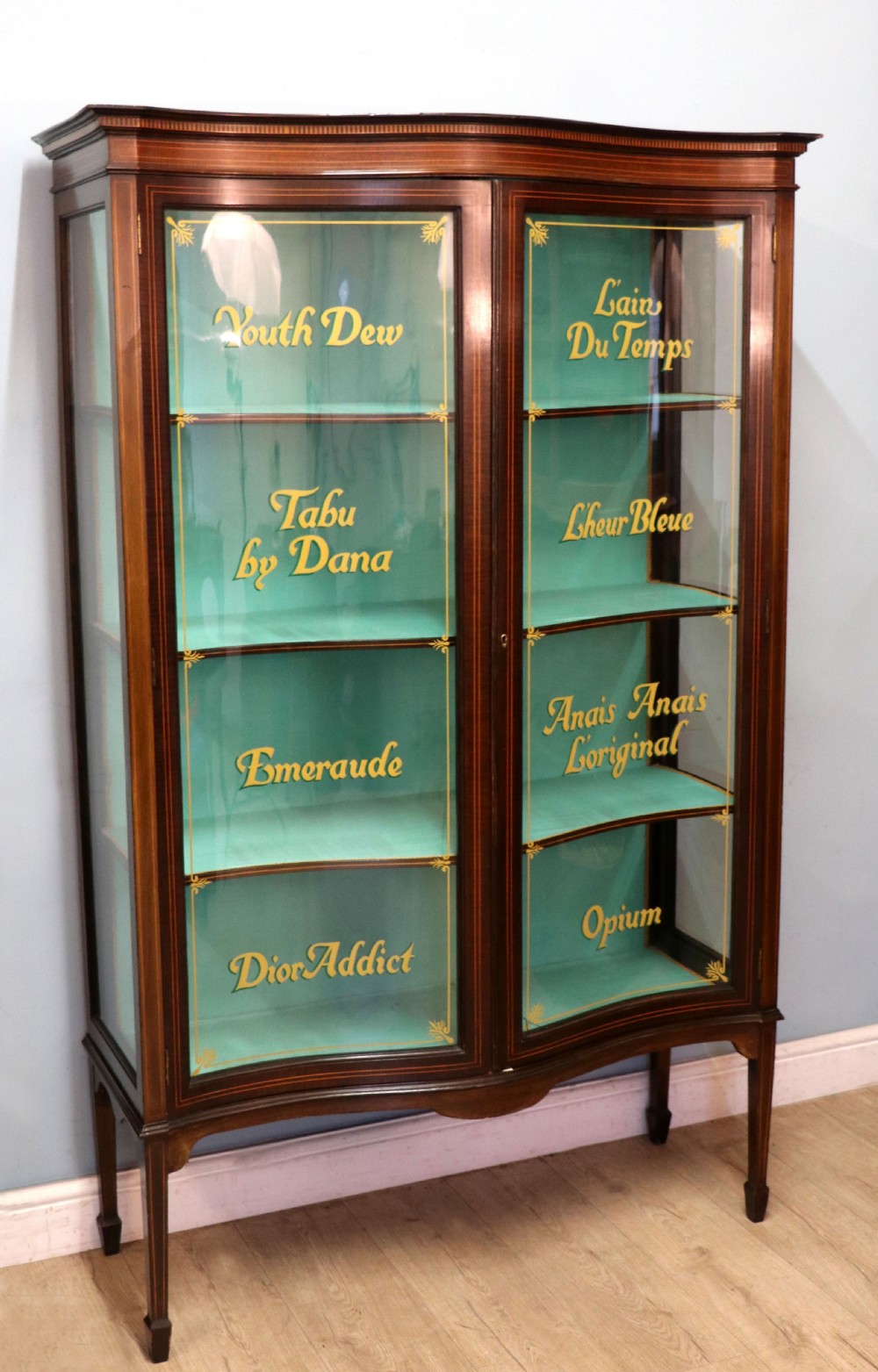 An Edwardian mahogany display cabinet featuring double glazed doors with gold sign-written perfume brand names against a turquoise painted interior. View III